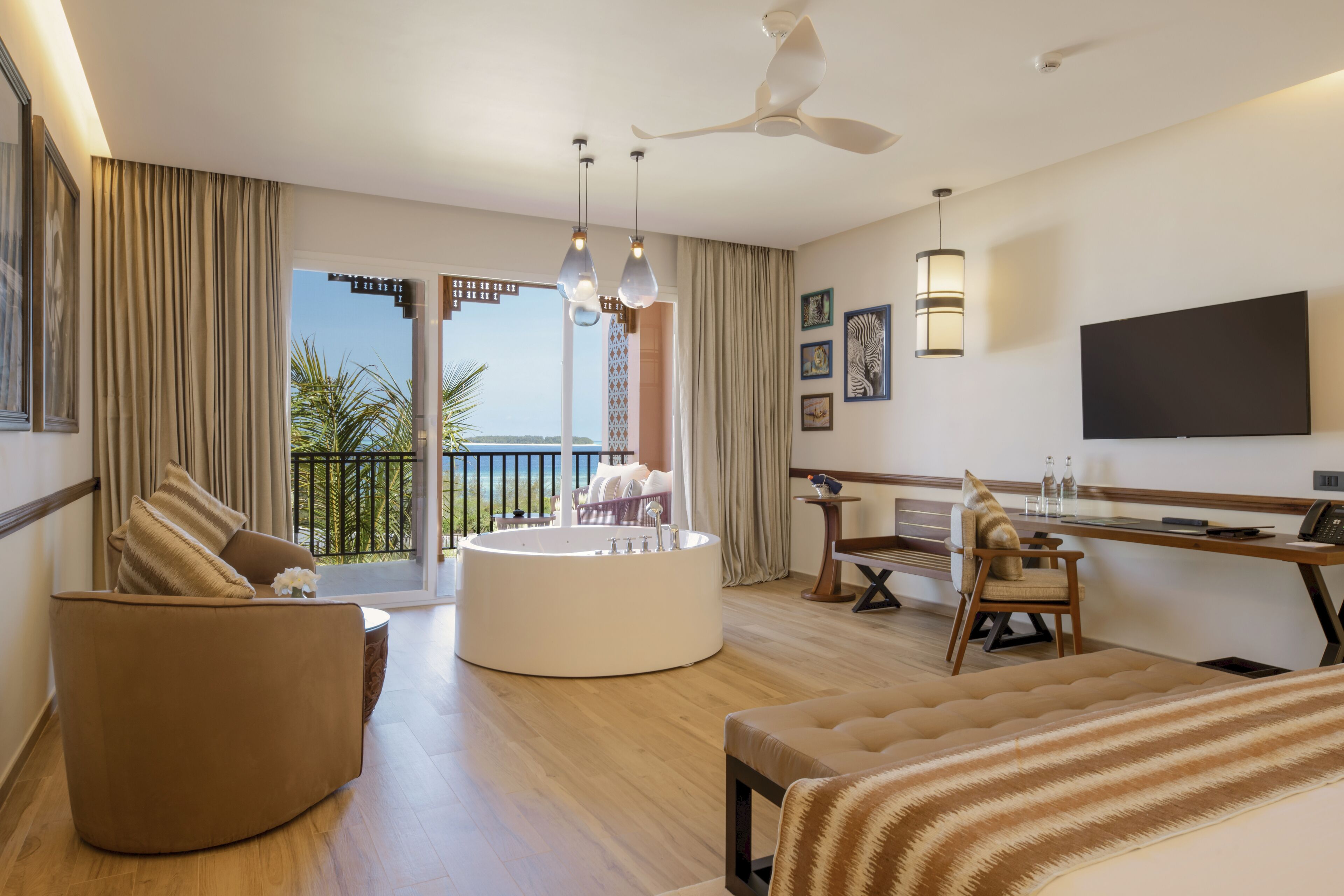 A modern hotel room with a round bathtub, a sofa, a desk, and a TV.