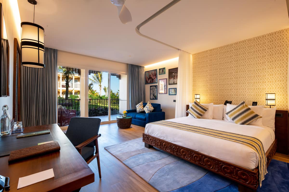 Habitación de hotel con una cama grande, un escritorio, una silla, un balcón con vistas a palmeras y una pared con diseño.