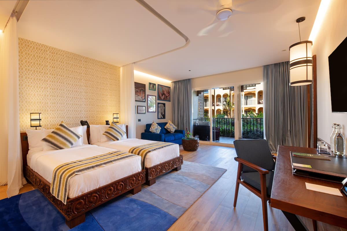 Habitación de hotel con cama doble, sofá, escritorio y balcón con vistas.