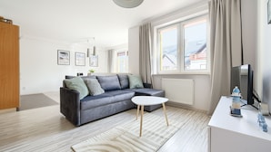 Una sala moderna con un sofá gris, una mesita auxiliar blanca y un televisor sobre un mueble.