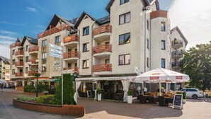 Un hotel de varios pisos con balcones, asientos exteriores y un letrero de una cafetería.