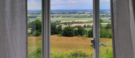 Vista a través de una ventana con cortinas, mostrando un paisaje rural con campos y árboles.