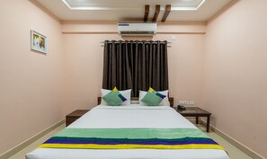 A hotel room with a bed, a bedside table with a phone, an air conditioning unit, a curtain, and a wall-mounted picture. - Treebo Eco Stay T Nagar (Chennai)