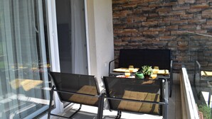 A balcony with two chairs, a table with drinks and a plant, and a brick wall. - Apartment Vapor (Dubrovnik)