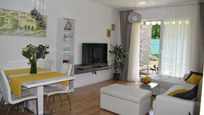 A modern living room with a dining area, a flat-screen TV, and a large window with curtains. - Apartment Vapor (Dubrovnik)
