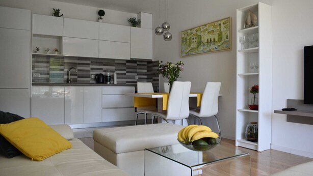 A modern living room with a sofa, coffee table, and a dining area with chairs and a table. - Apartment Vapor (Dubrovnik)