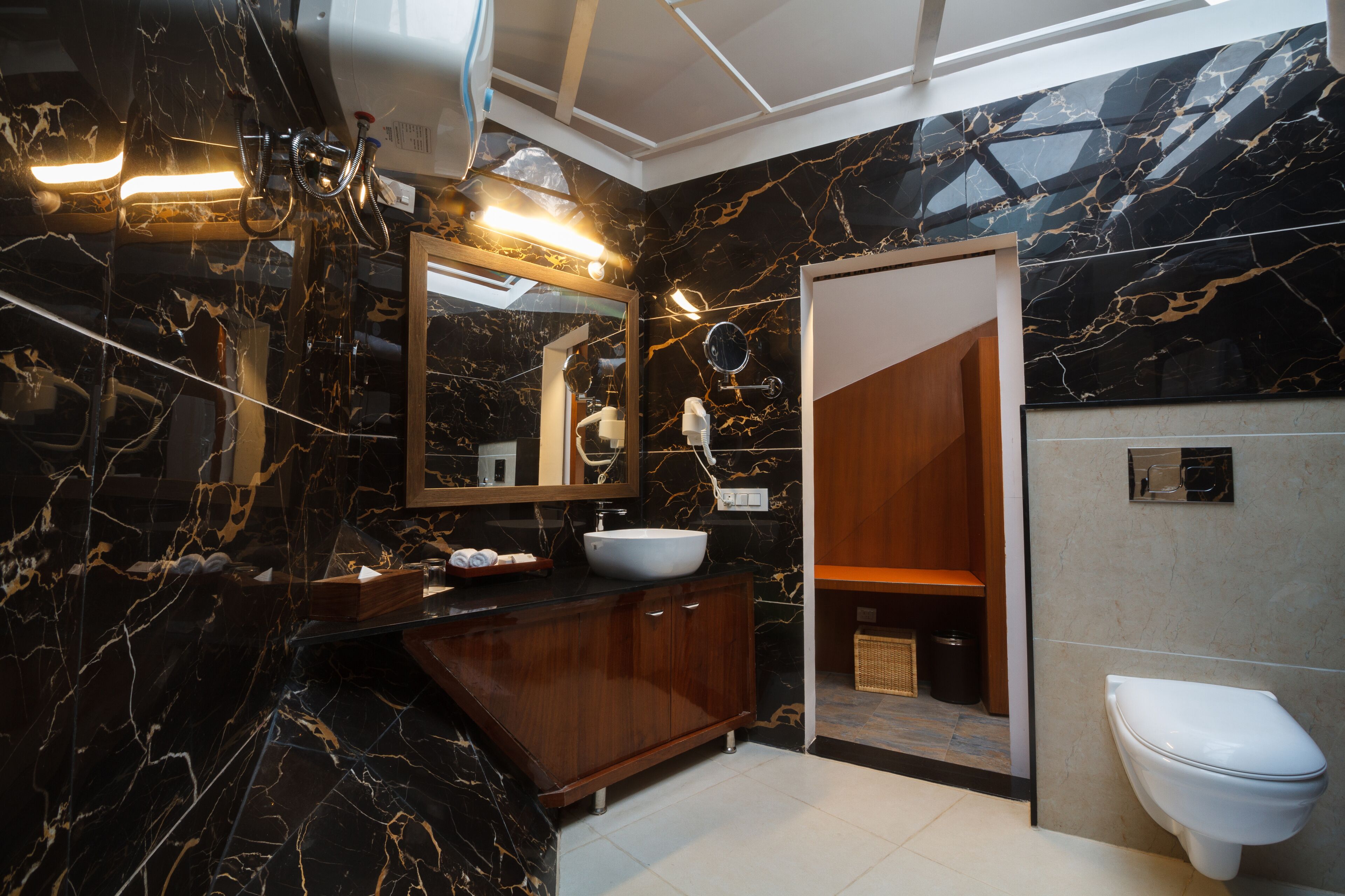 Un baño moderno con lavamanos de mármol, tocador de madera y un inodoro blanco.
