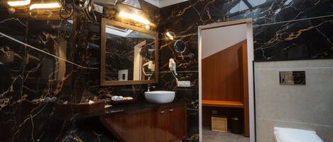 Un baño moderno con lavamanos de mármol, tocador de madera y un inodoro blanco.