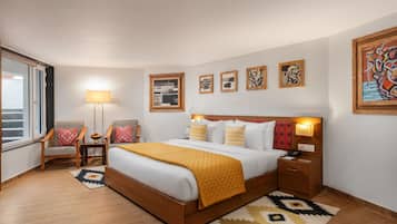 Une chambre d’hôtel avec un lit en bois, deux chaises, une table de chevet, une lampe et des œuvres d’art accrochées aux murs.