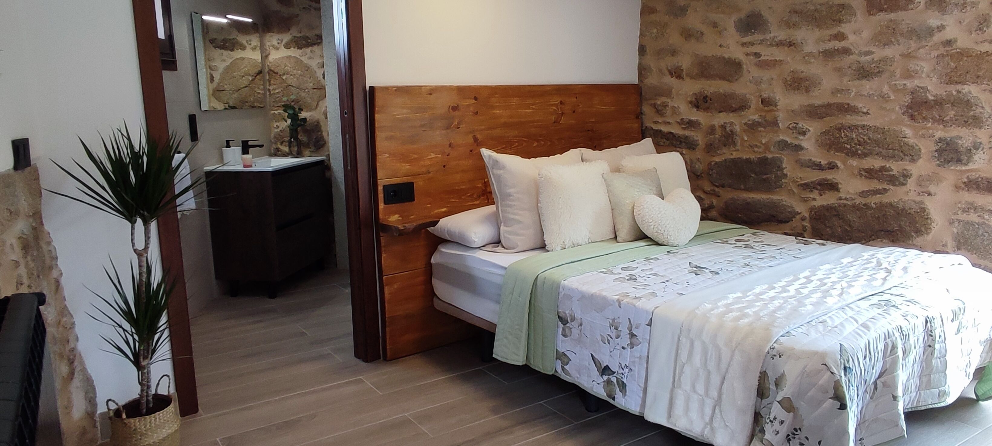 Une chambre à coucher avec une tête de lit en bois, un lit avec une literie blanche, une table de chevet, une commode et un mur en pierre.