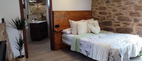 Une chambre à coucher avec une tête de lit en bois, un lit avec une literie blanche, une table de chevet, une commode et un mur en pierre.