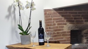 Una mesa de madera con dos sillas, una orquídea en maceta, una botella de vino y una copa sobre la mesa.