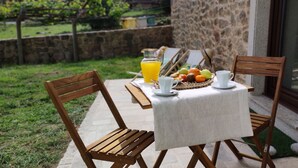 Mesa al aire libre con un muro de piedra de fondo, una cesta de mimbre con frutas y una jarrón de zumo de naranja.