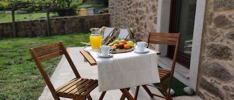 Ein Tisch draußen mit einer Steinschutzmauer im Hintergrund, einem Korbwannen-Korb mit Früchten und einem Krug Orangensaft.