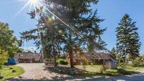 A building with a tiled roof, a gravel driveway, and a large tree in the foreground. - Vacation village house 63b (Ostseebad Boltenhagen)