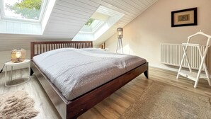 A bedroom with a wooden bed, skylights, a radiator, and a hanging light fixture. - Vacation village house 63b (Ostseebad Boltenhagen)