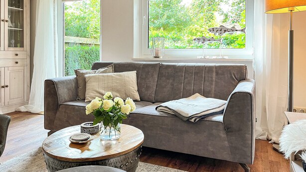 A living room with a grey sofa, a round coffee table, and a vase of white flowers. - Vacation village house 63b (Ostseebad Boltenhagen)