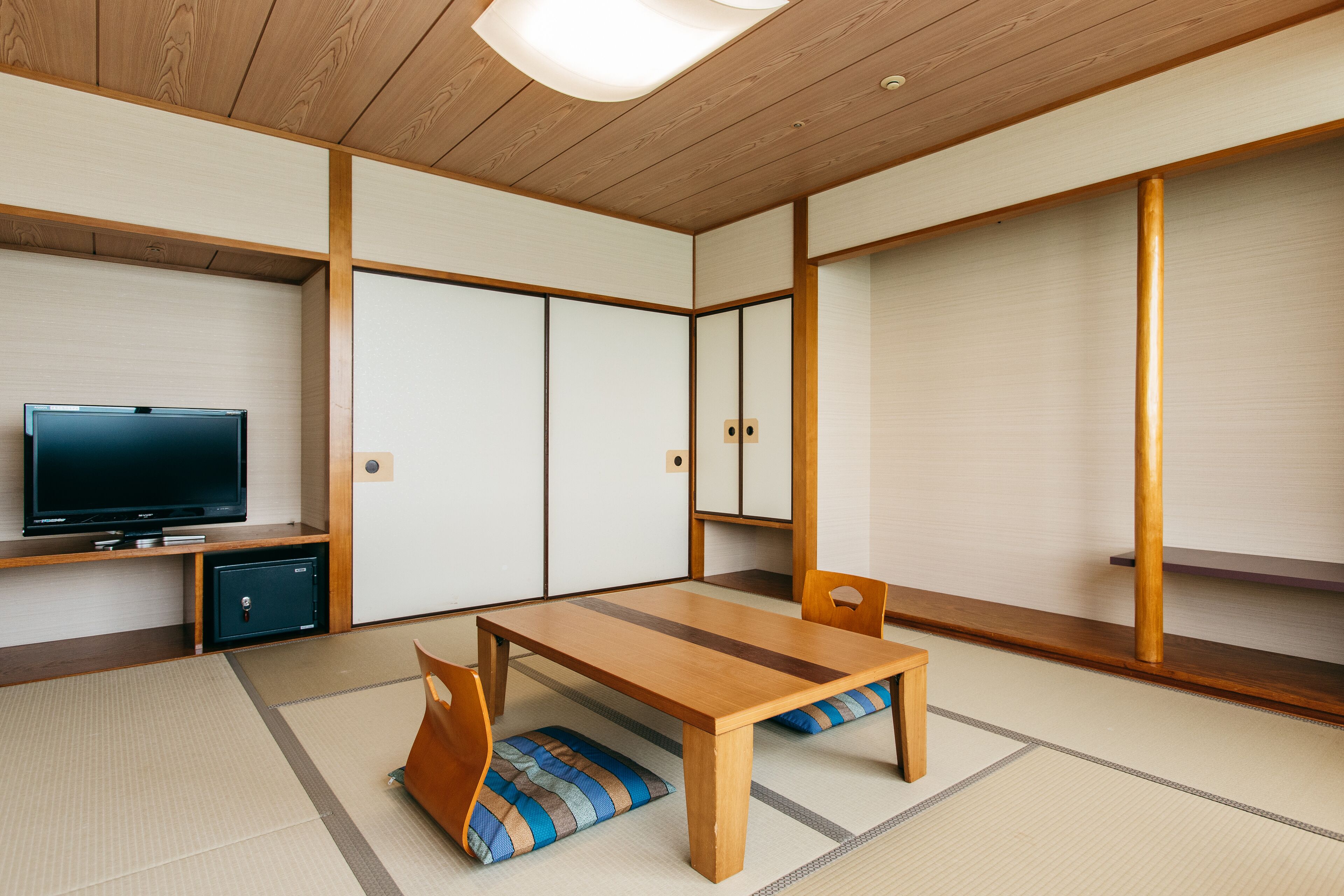 A traditional Japanese room with tatami flooring, a low wooden table, and a television on a shelf.