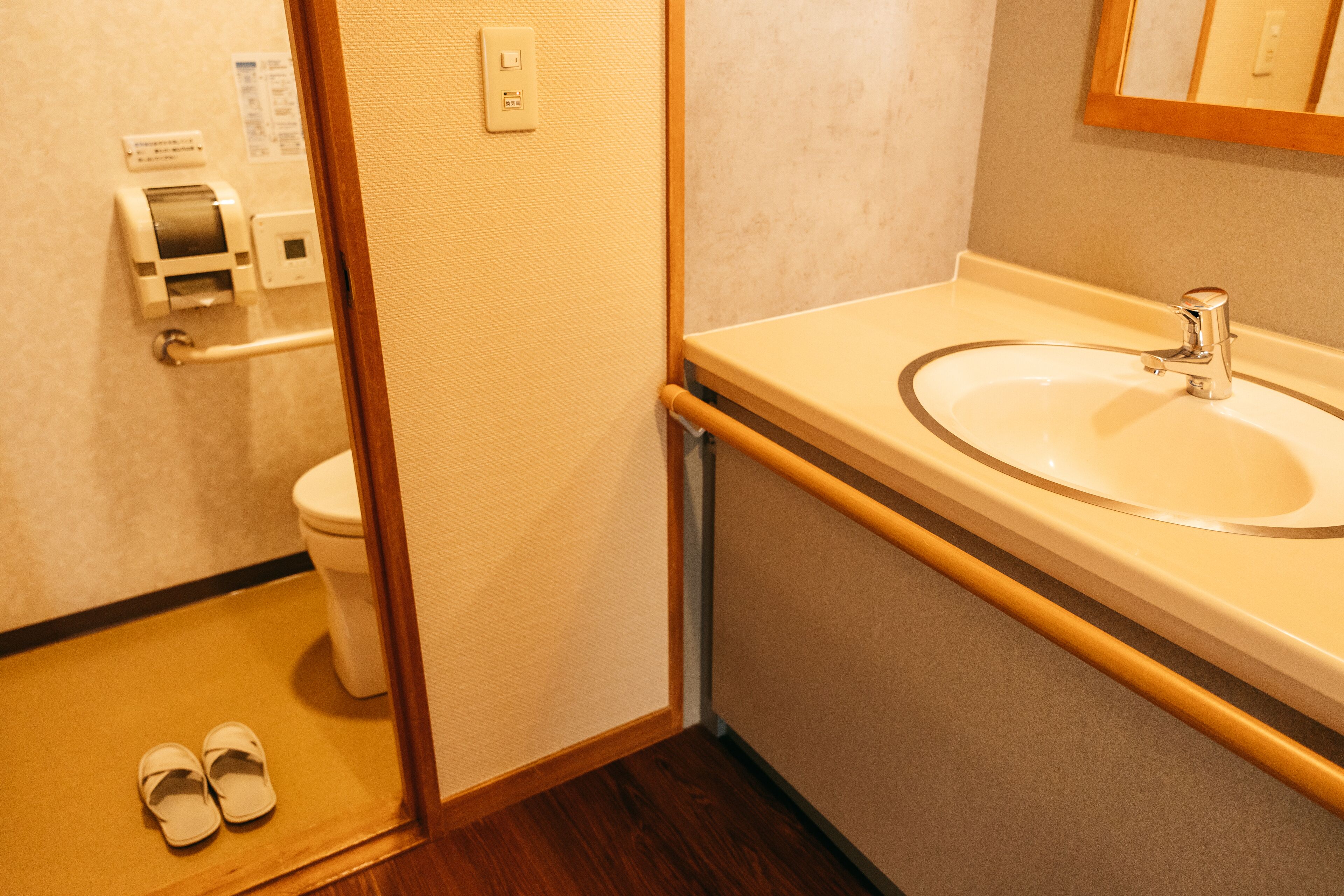 A bathroom with a sink, toilet, and a pair of slippers on the floor.