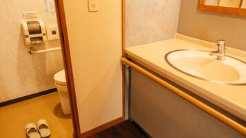 A bathroom with a sink, toilet, and a pair of slippers on the floor.