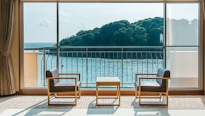 Un balcon avec deux chaises et une petite table, donnant sur une étendue d’eau et une colline boisée.