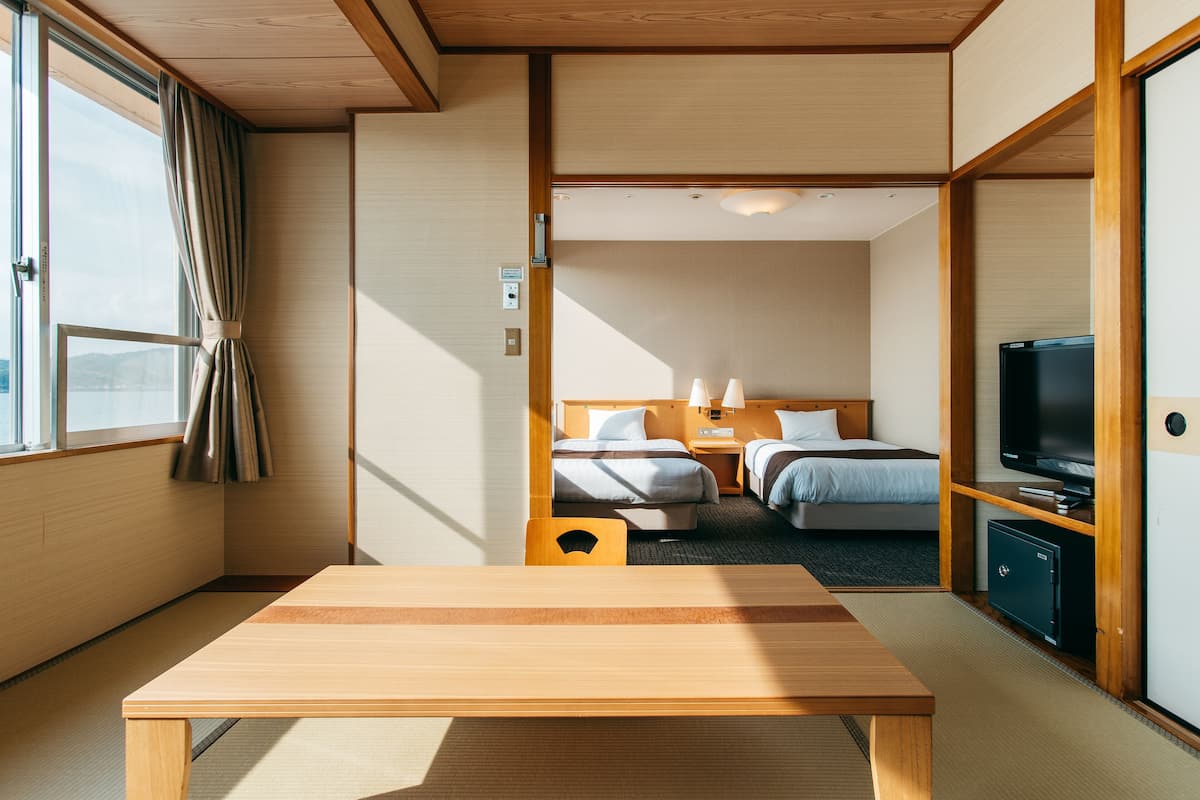 Ein Hotelzimmer mit Holztisch, zwei Betten, einem Fernseher und Blick ins Freie.