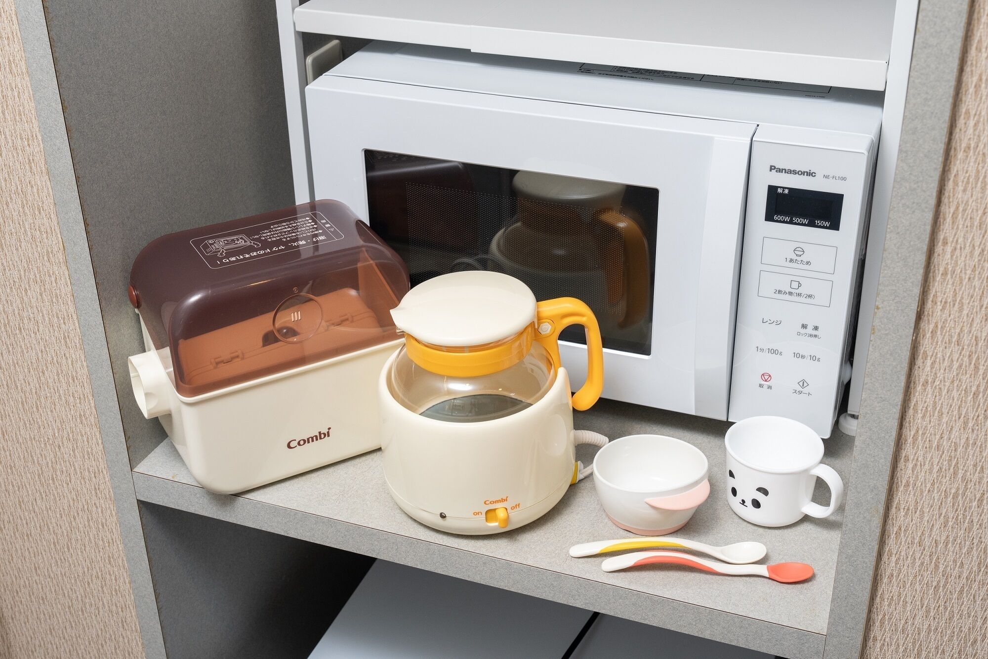 A microwave with a control panel, a coffee maker, a mug, and a spoon set on a countertop.