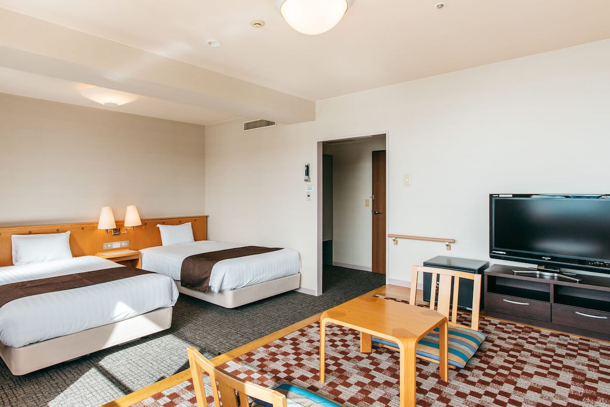Ein Hotelzimmer mit zwei Betten, einem Fernseher, einem kleinen Tisch und einem Schlafsofa.