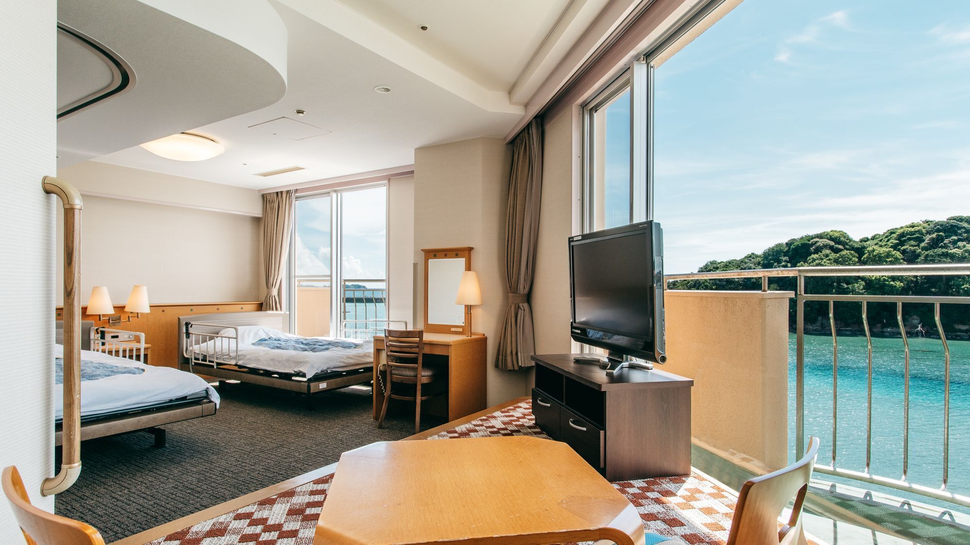 Une chambre d’hôtel avec deux lits, une télévision, un bureau et un balcon donnant sur la mer.