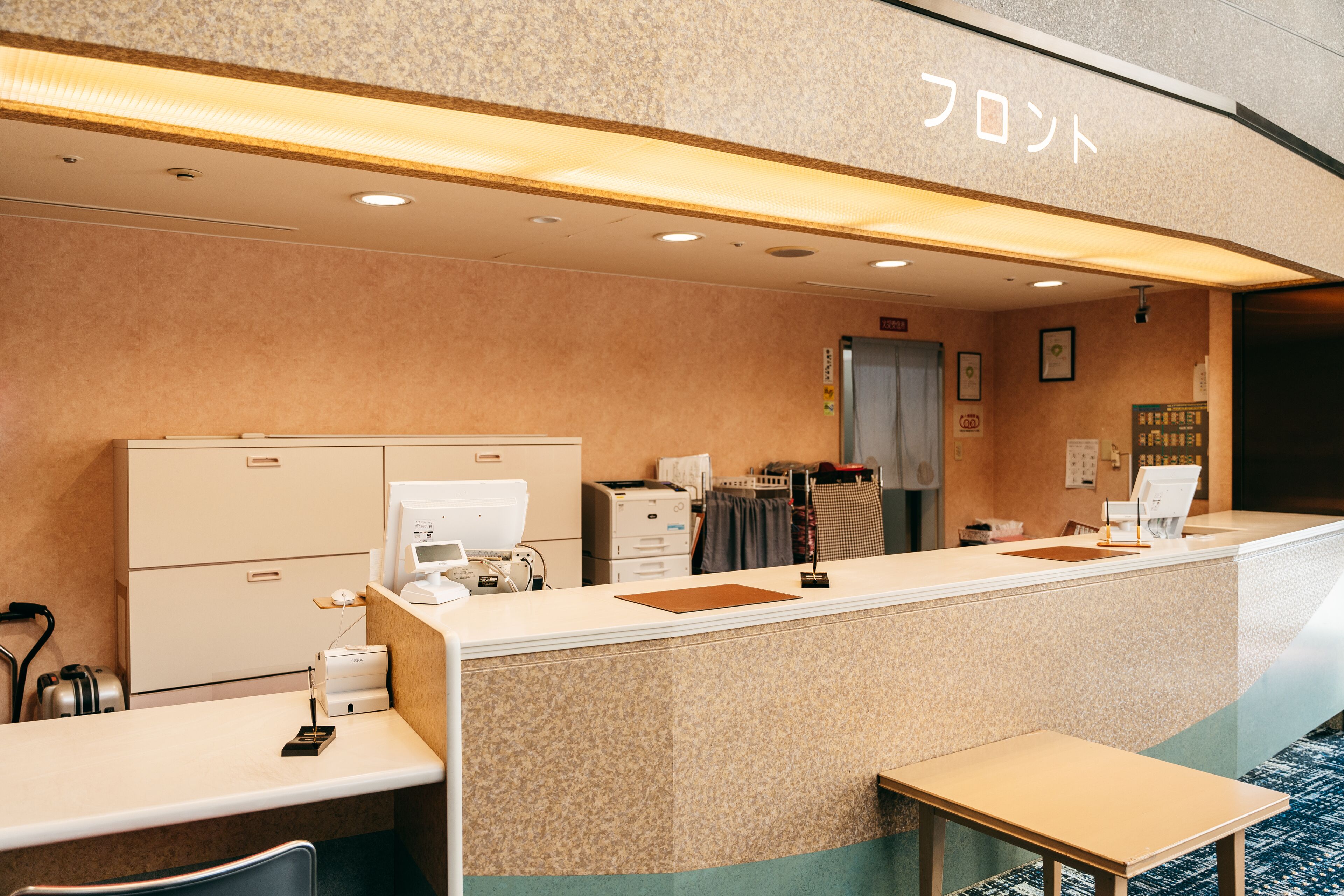 A hotel reception area with a counter, a coffee machine, a printer, and a small seating area.