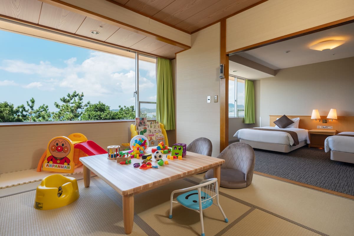Ein Hotelzimmer mit Balkon, einem Bett, einem Schreibtisch mit Spielzeug und Blick ins Grüne.