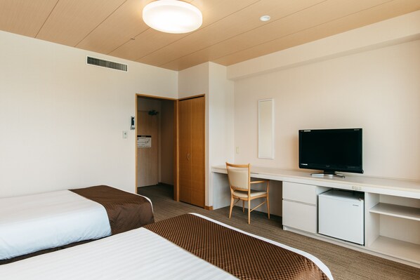 Una habitación de hotel con dos camas, un escritorio con televisor, una silla y un refrigerador pequeño.