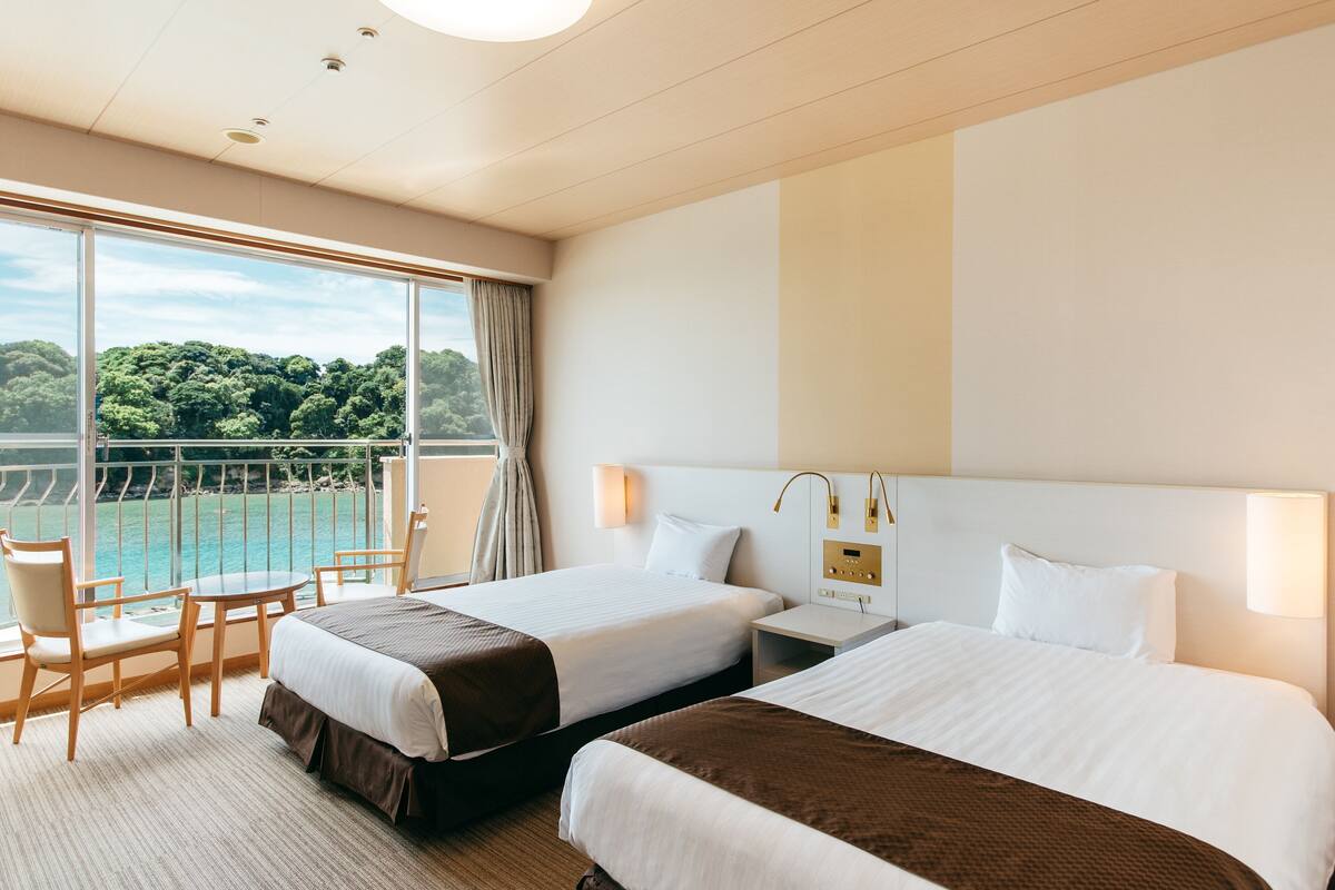 Ein Hotelzimmer mit zwei Betten, einem Balkon mit Meerblick und einem Tisch mit Stühlen.