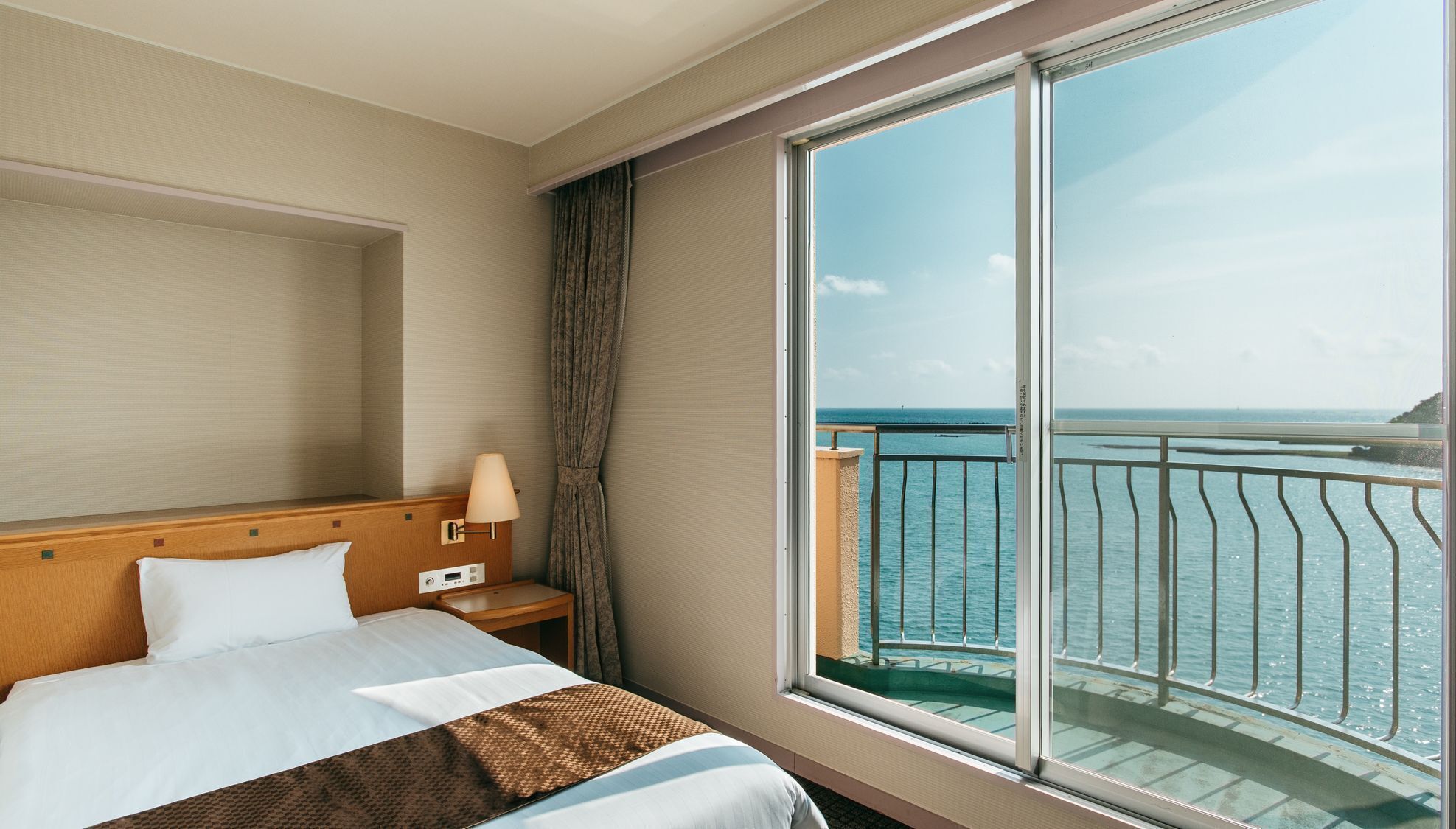 Une chambre d’hôtel avec une grande fenêtre, un lit, une table de chevet et une lampe.