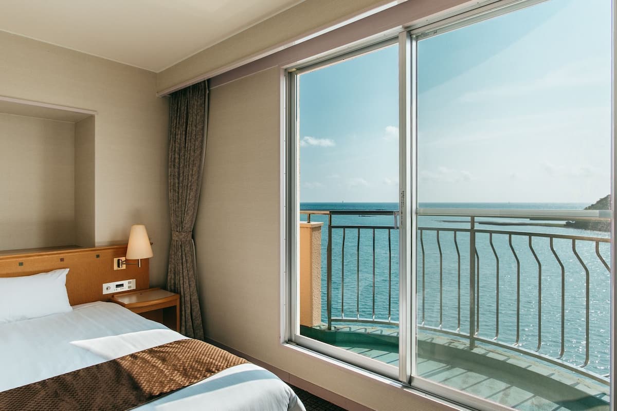 Ein Hotelzimmer mit großem Fenster, einem Bett, einem Nachttisch und einer Lampe.