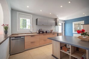 A modern kitchen with a dishwasher, wooden cabinets, a countertop with a coffee maker, and a window.