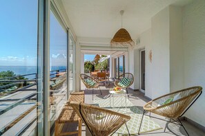 A balcony with wicker furniture, a table with fruit, and a view of the sea.