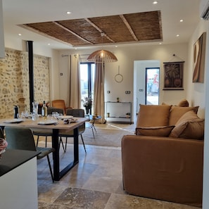 Un salon moderne avec un coin repas, agrémenté d’un mur en pierre, d’un plafond en bois et d’une grande fenêtre.