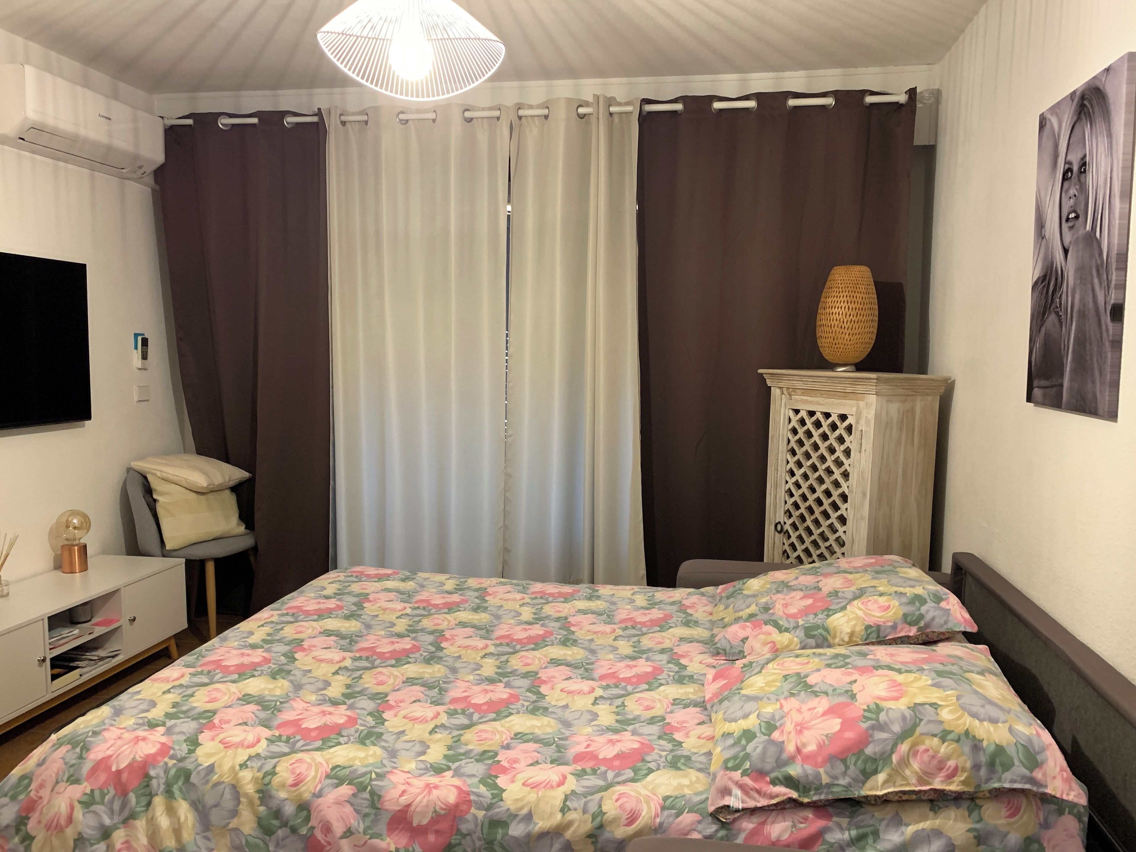 A bedroom with a bed, a bedside table with a lamp, a wardrobe, and a wall-mounted TV.