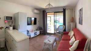 A living room with a red sofa, a television, a small table, a wicker chair, and a sliding glass door leading to a balcony. - Nice view - PORT GRIMAUD (Grimaud)