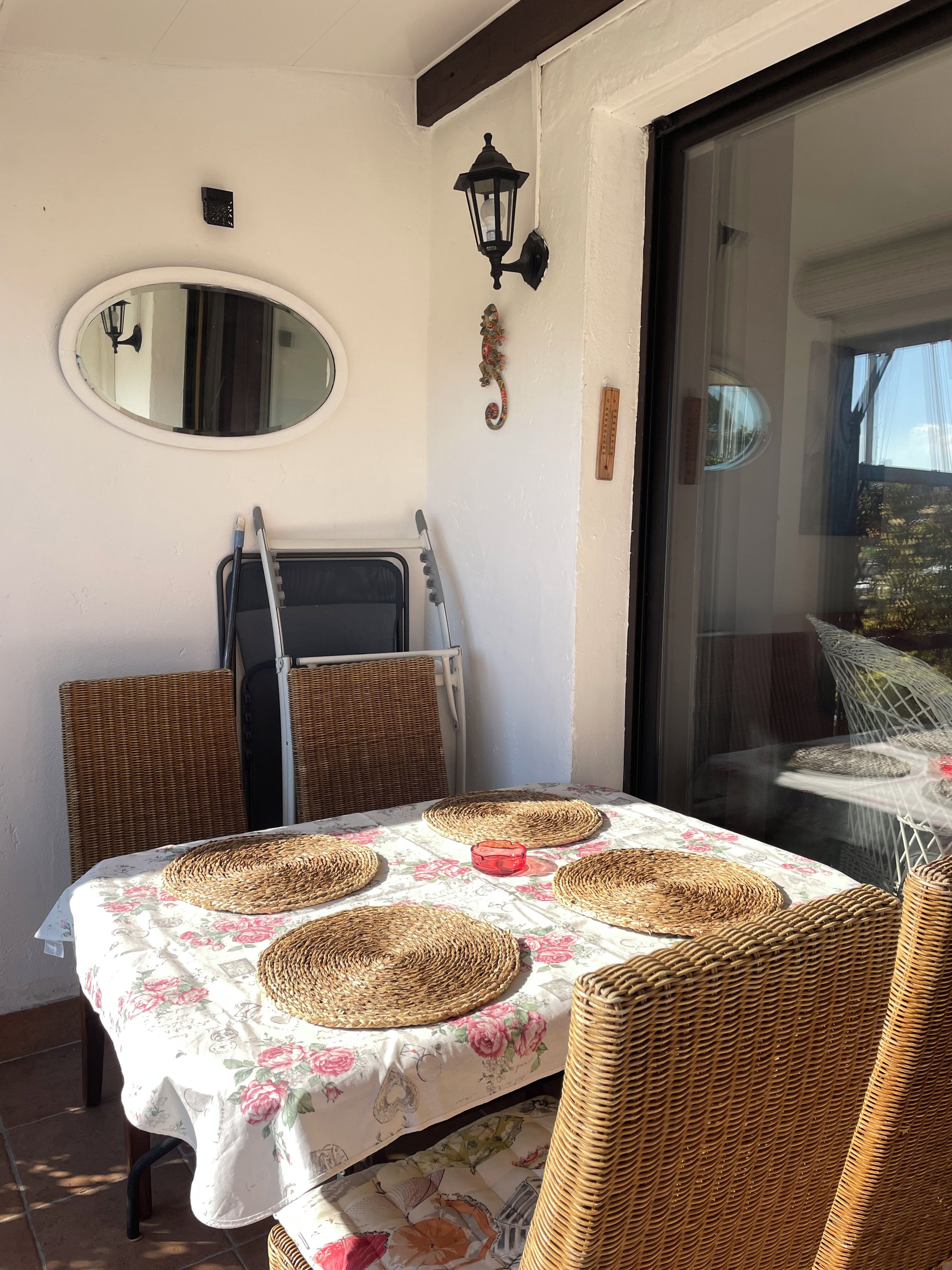 A dining area with wicker chairs, a table with a floral tablecloth, and a large mirror on the wall.