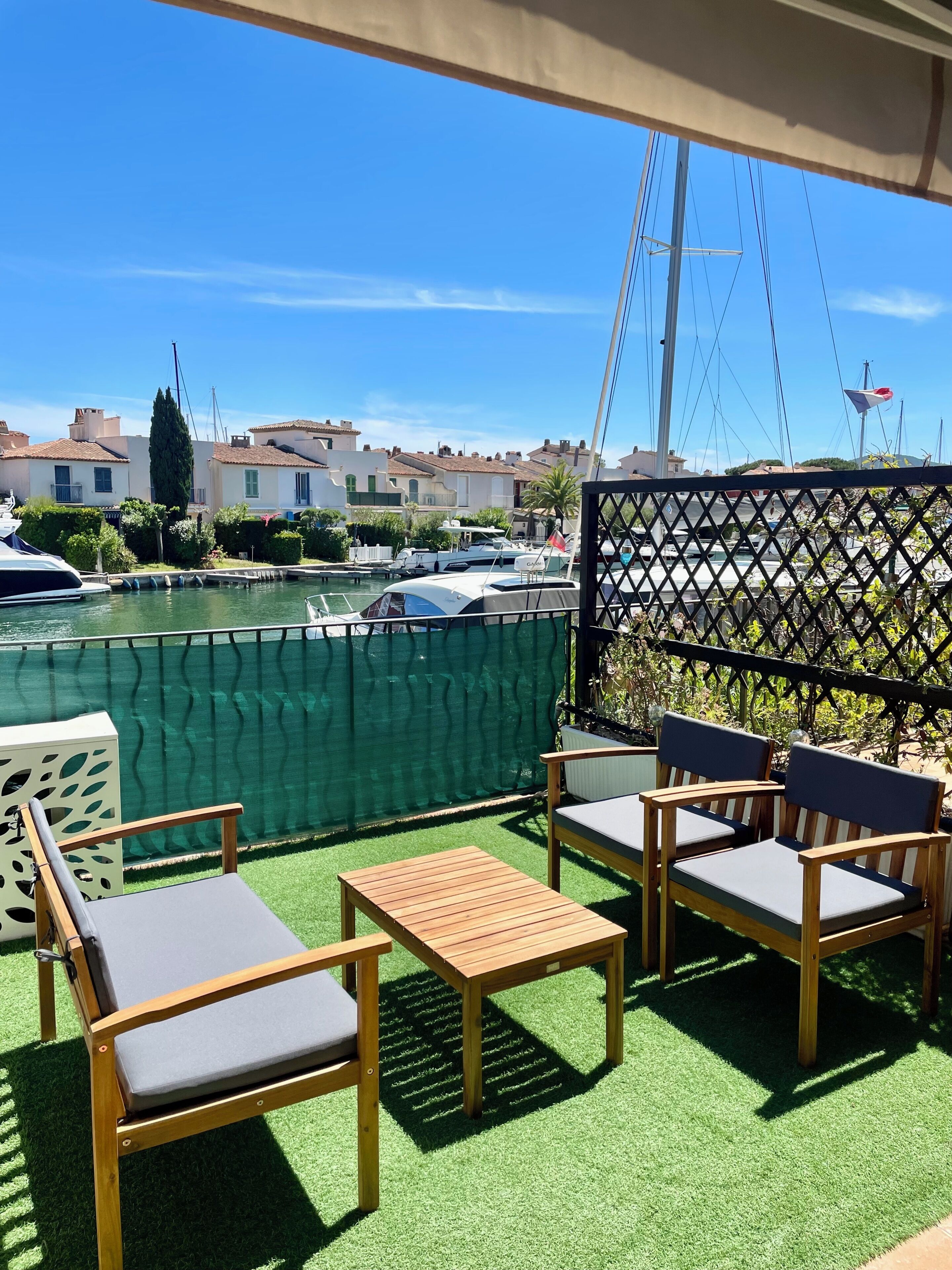 Eine Terrasse mit Gartenmöbeln, Blick auf eine Marina mit Booten und eine Reihe von Gebäuden im Hintergrund.