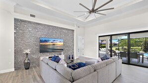 A modern living room with a gray sectional sofa, a flat-screen TV mounted on a stone wall, and a ceiling fan.