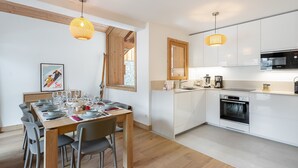 A modern kitchen with white cabinets, a built-in oven, and a dining area with a wooden table and chairs.