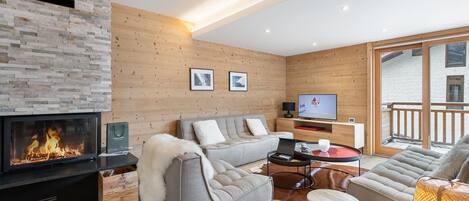 Un salon moderne avec une cheminée, des murs en bois, un canapé, un téléviseur et une vue sur l’extérieur.