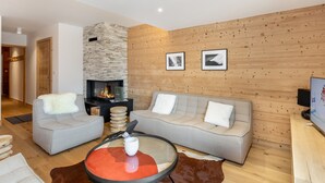 A modern living room with a stone fireplace, grey sofas, a coffee table, and wooden paneling on the walls.
