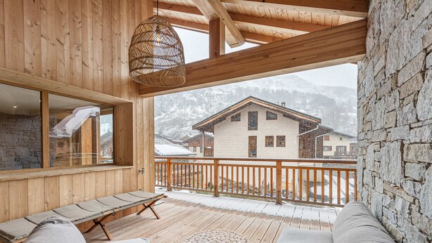 A wooden deck with a sofa, a round wooden coffee table, and a hanging light fixture.
