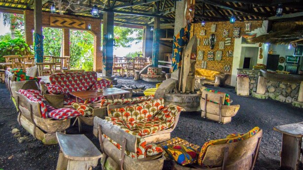 An outdoor seating area with rustic wooden furniture and a thatched roof. - Paradis Malahide (Nyayumba)
