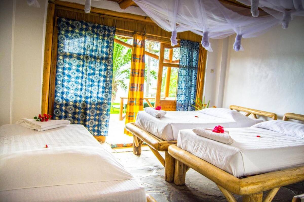 A room with two wooden beds, a large window with patterned curtains, and a canopy bed.