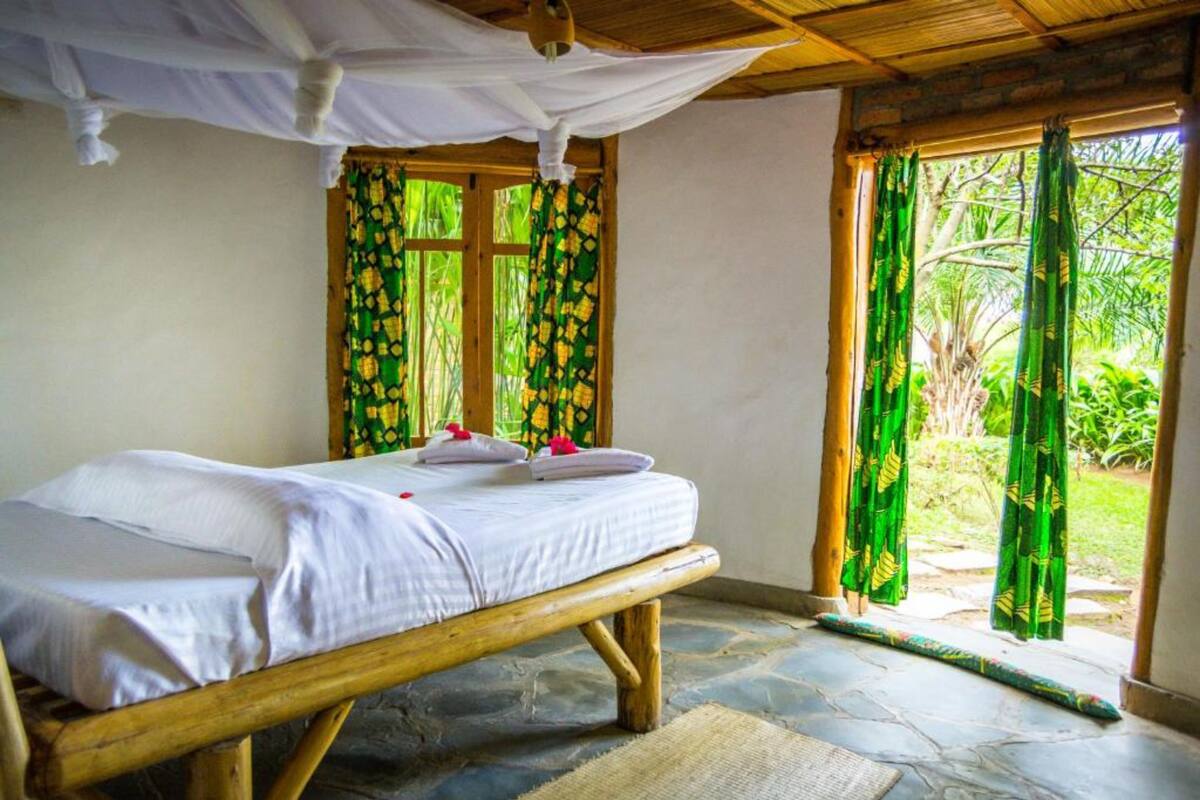 A room with a bed, a window with curtains, and a view of greenery outside.